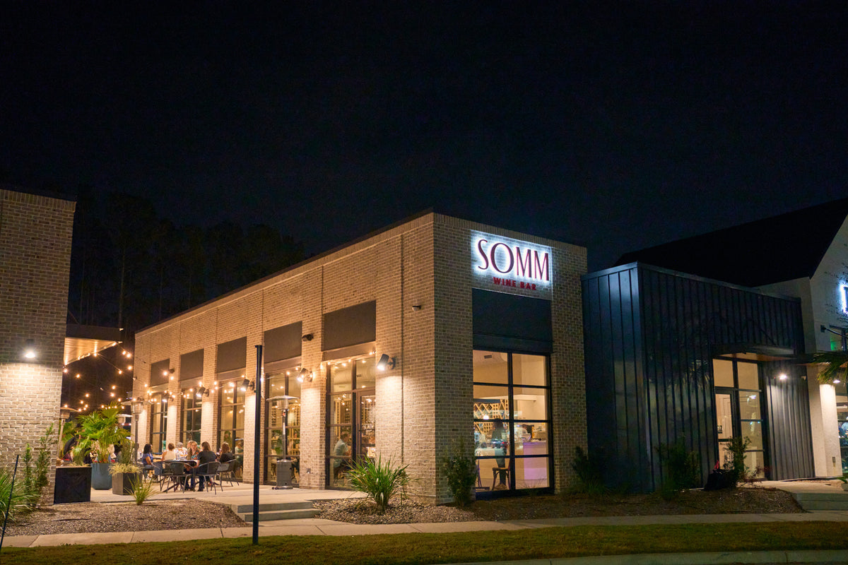 The brick exterior of SOMM Wine Bar at Nexton at dusk, with the illuminated SOMM sign above the entrance